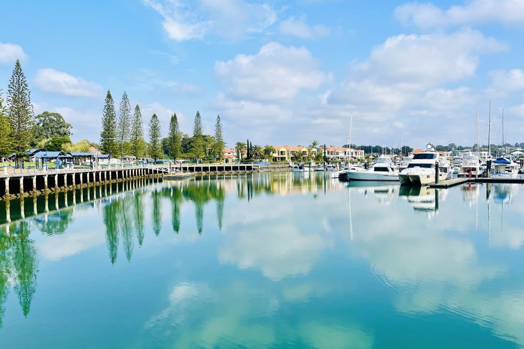 Marina. Boats in a harbour with trees and clouds reflected in the water.