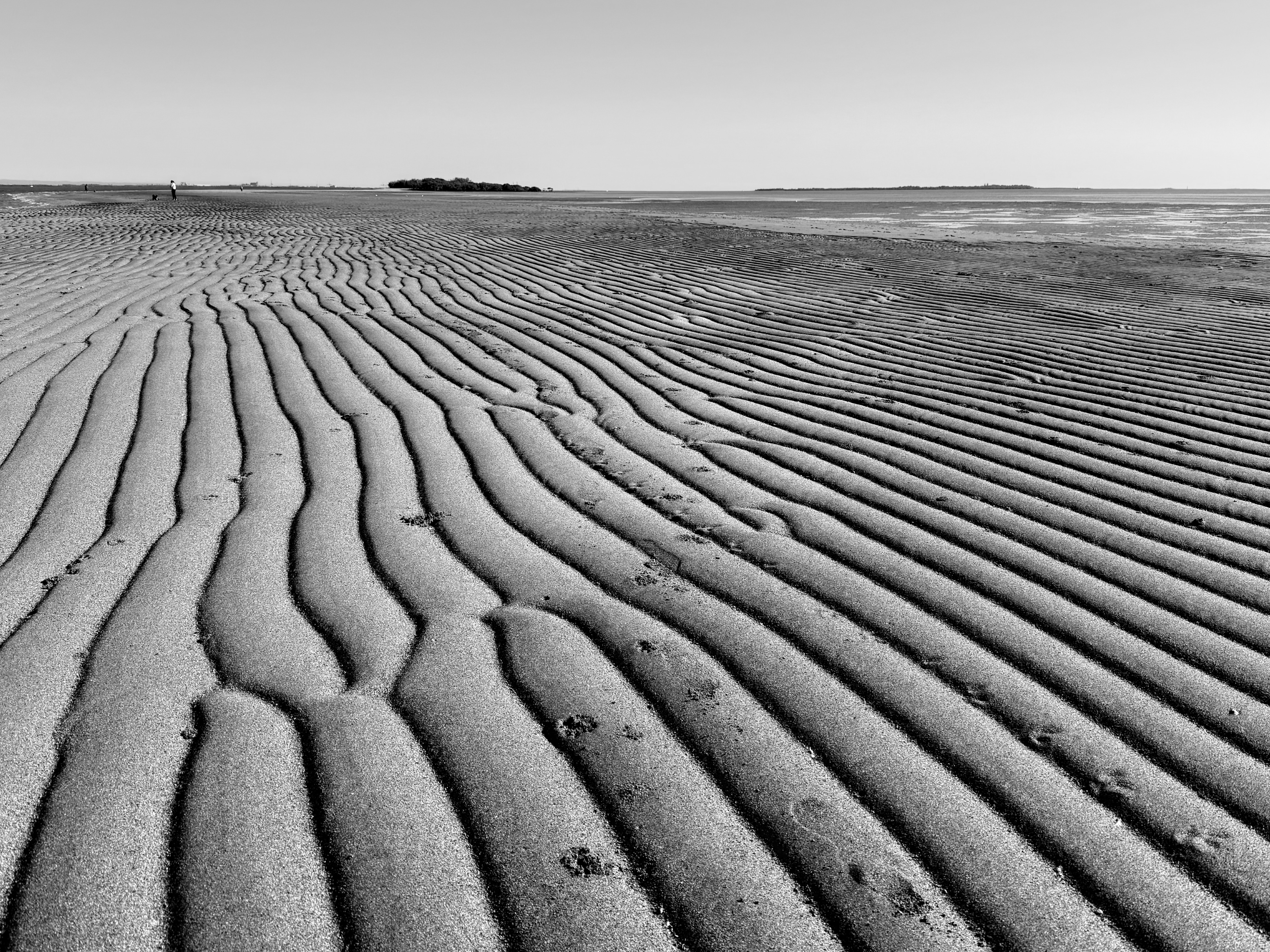 Ripples in sand on a beach, with footprints.