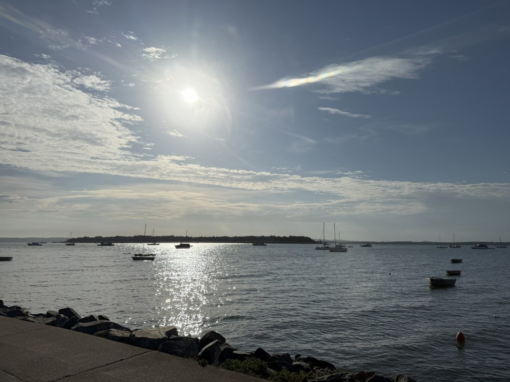 Sun bright in the sky, boats in the sea and water is shining.