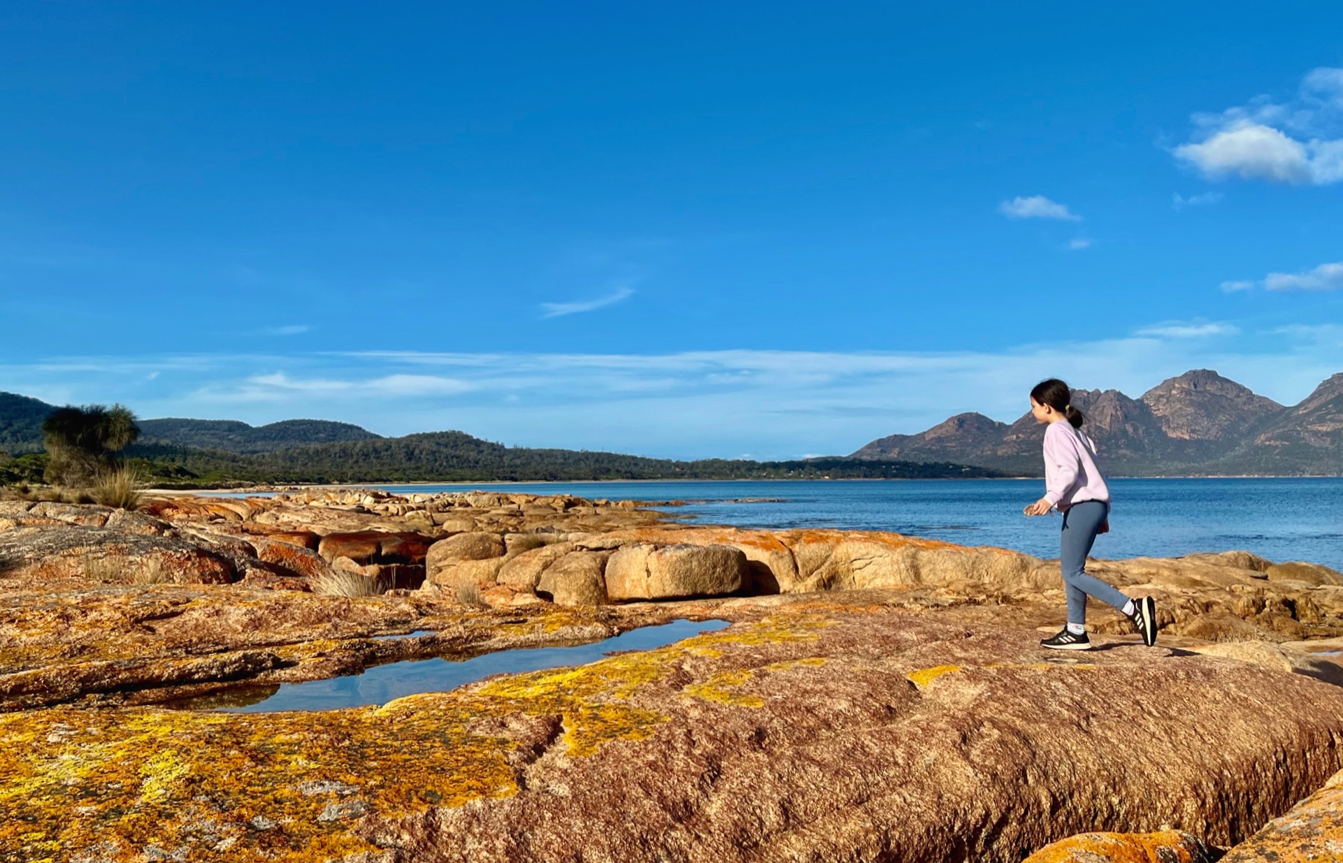 A girl walking along the top of orange rocks In Tasmania.