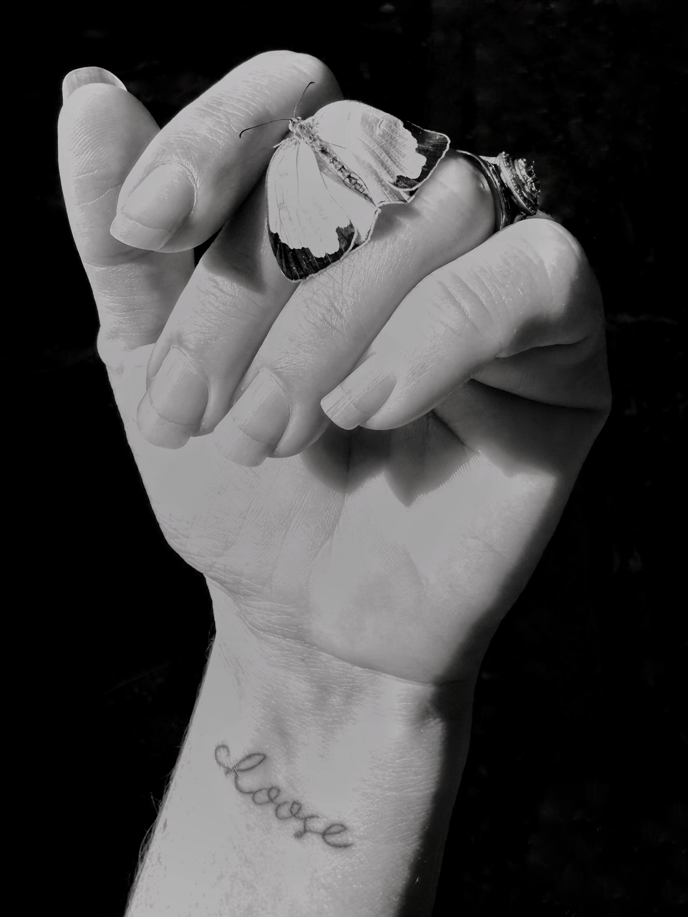 A human hand with a small butterfly on the fingers, and a tattoo on the wrist that reads: Choose.